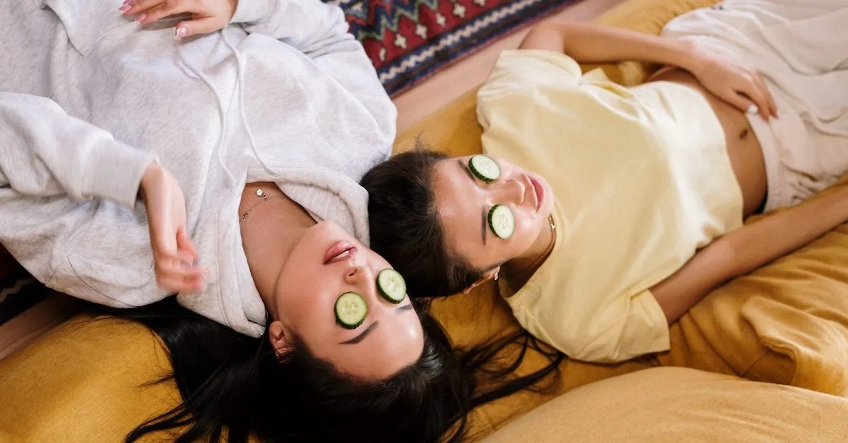 Hai cô gái nằm thư giãn với lát dưa leo đặt trên mắt trong không gian ấm cúng.
